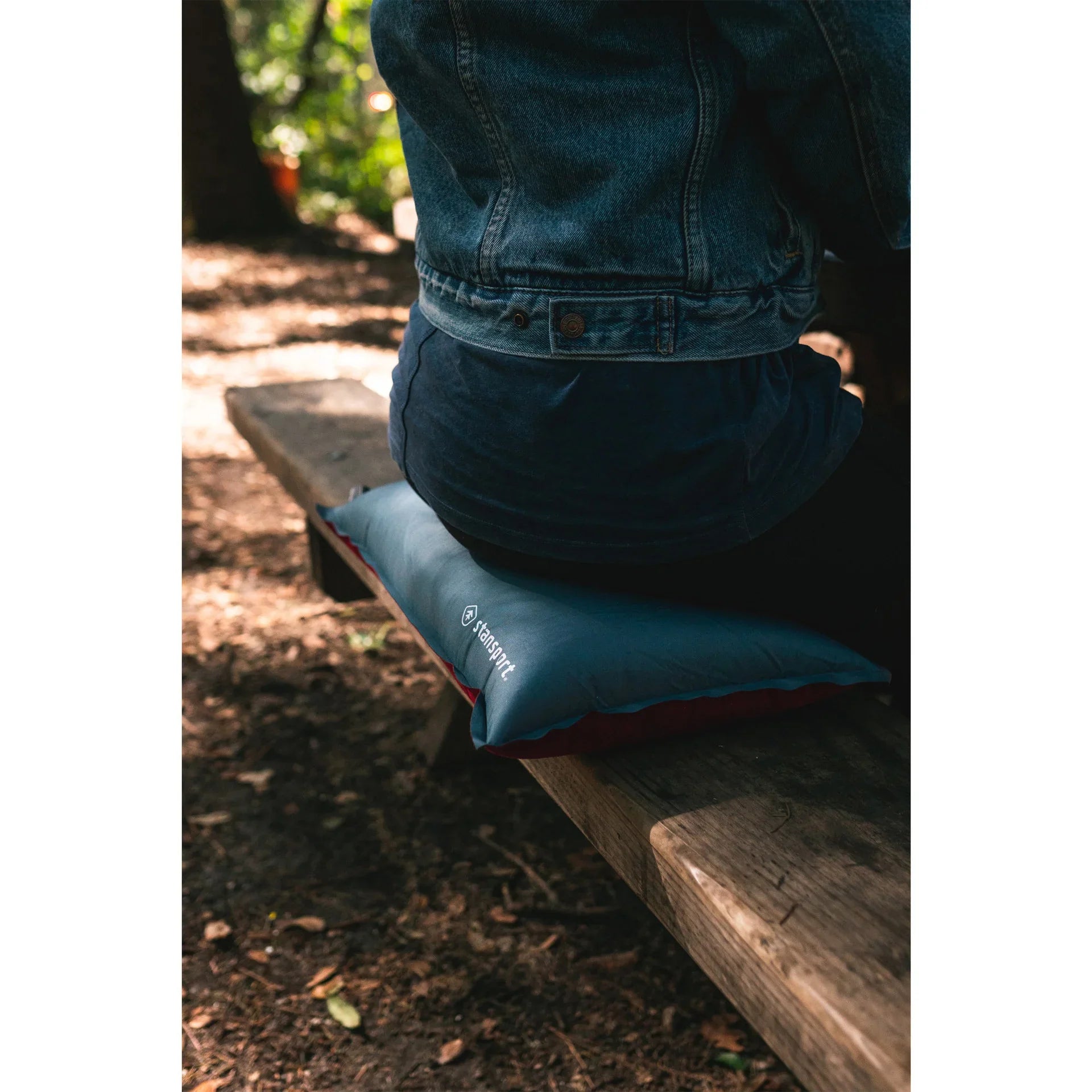 Person in denim jacket sitting on gear seat cushion on outdoor wooden bench