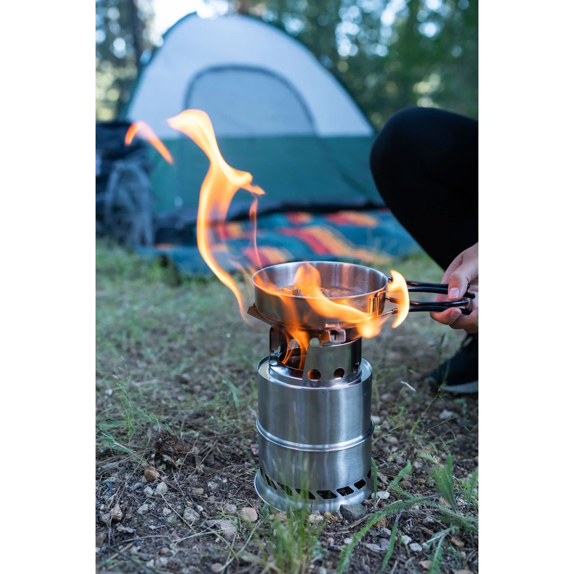 Camping stove with flames and pan outdoors near tent on grass