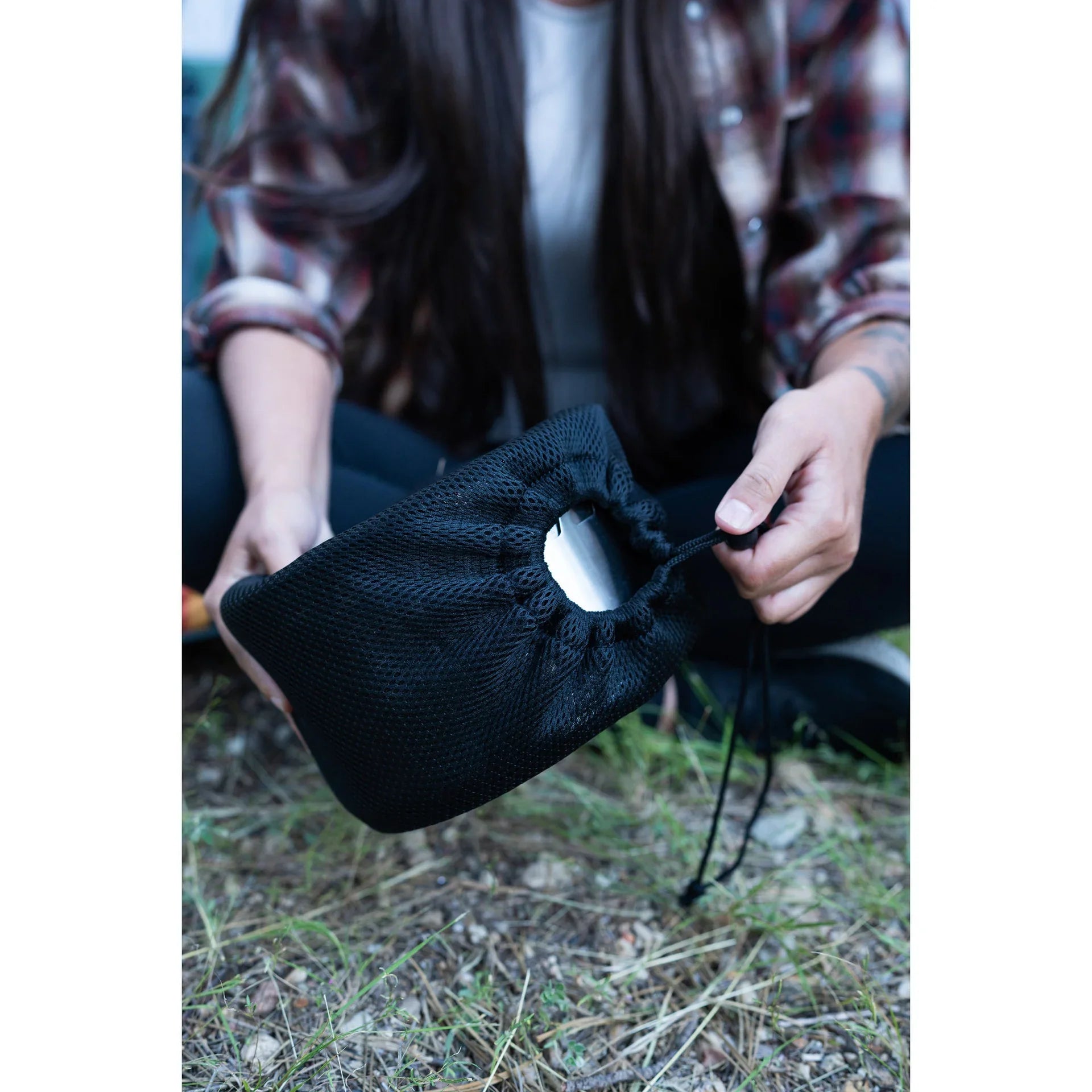 Camper holding black mesh drawstring pouch with toilet paper outdoors