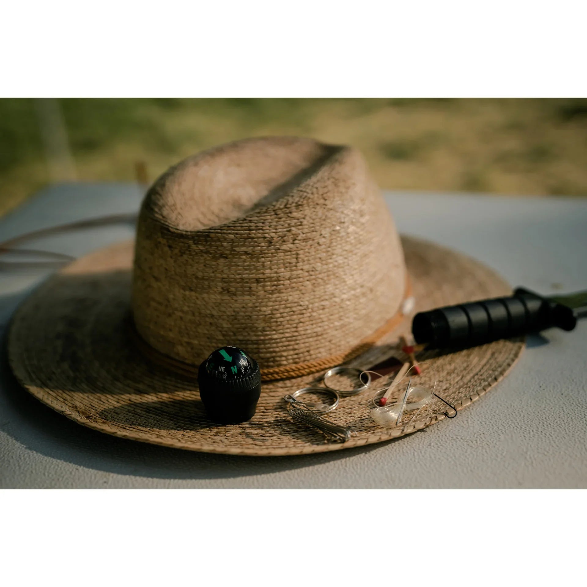 Outdoor adventure gear with straw hat, compass, survival knife, and small tools on table