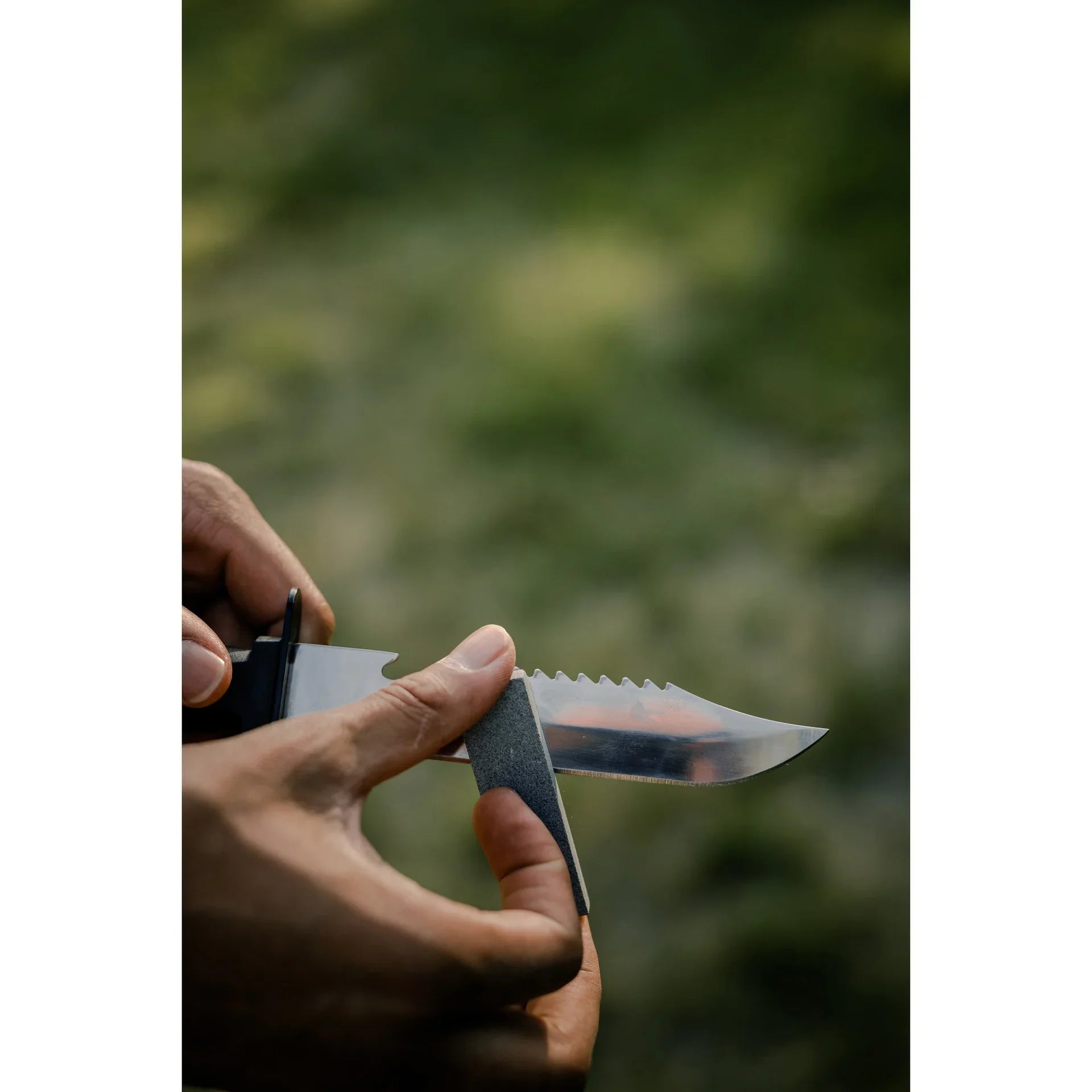 Hand sharpening a serrated survival knife outdoors with a sharpening stone