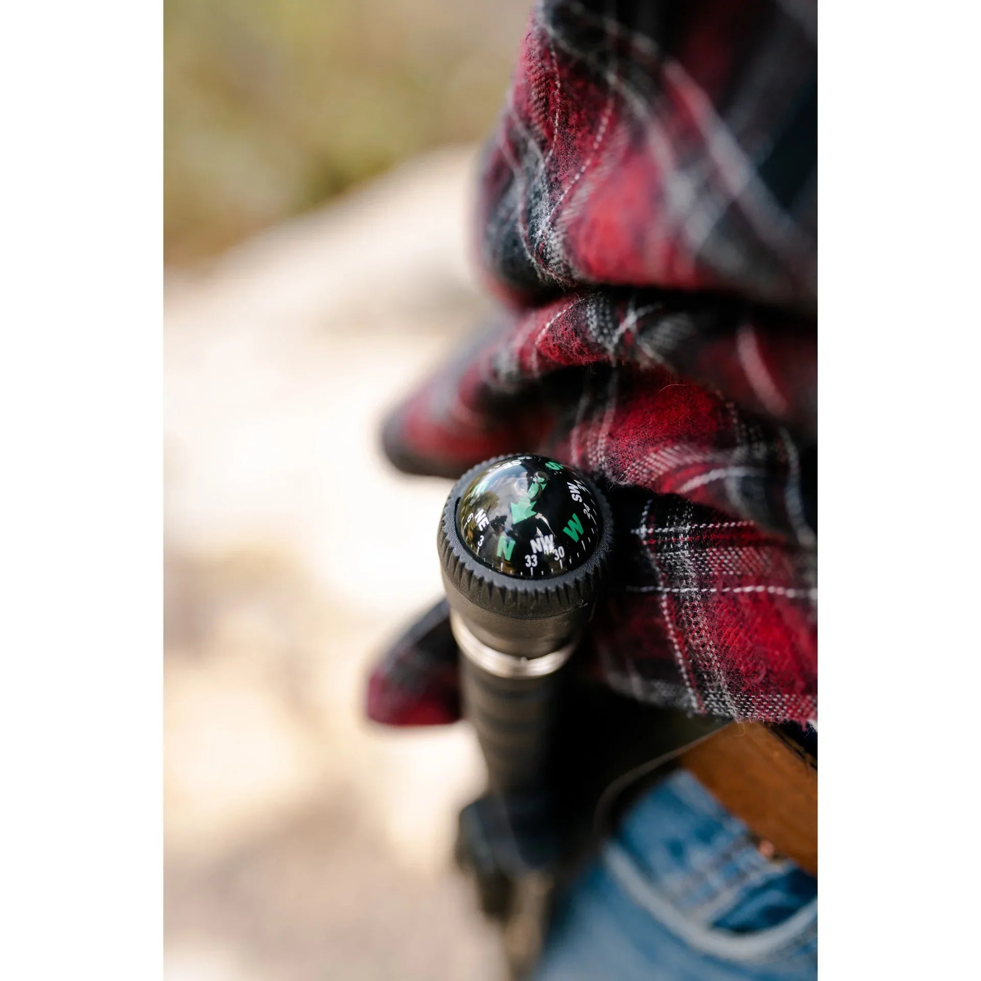 Outdoor close-up of black hiking stick with compass, next to red plaid shirt and jeans