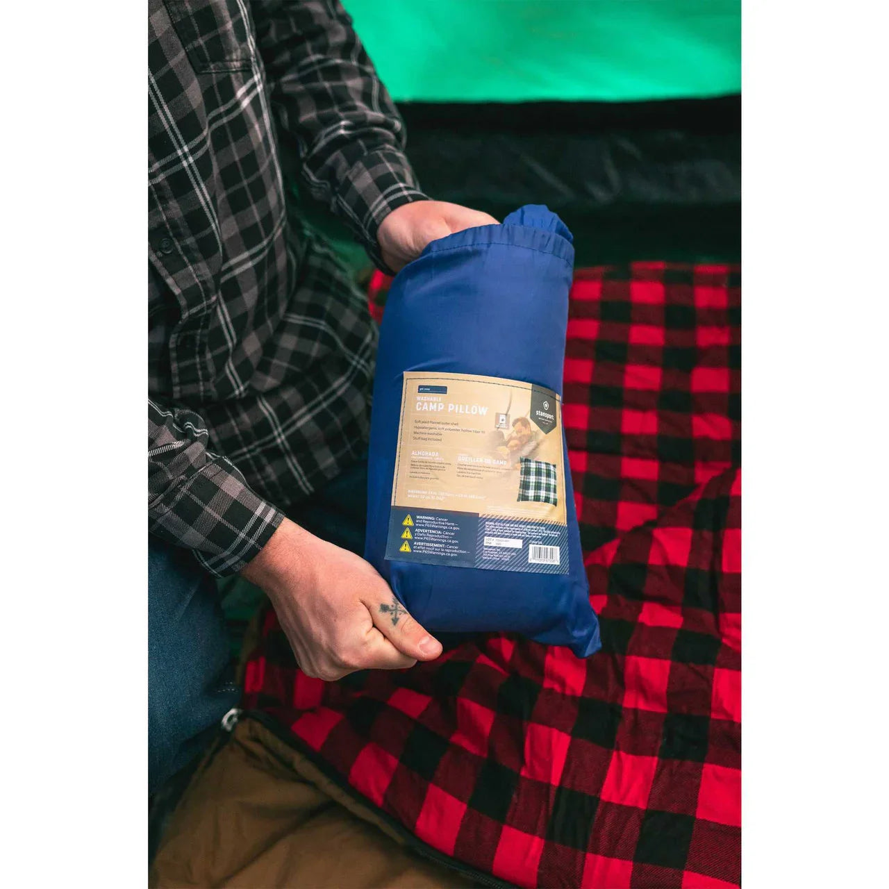 Person holding blue Stansport washable camp pillow on red plaid camping blanket