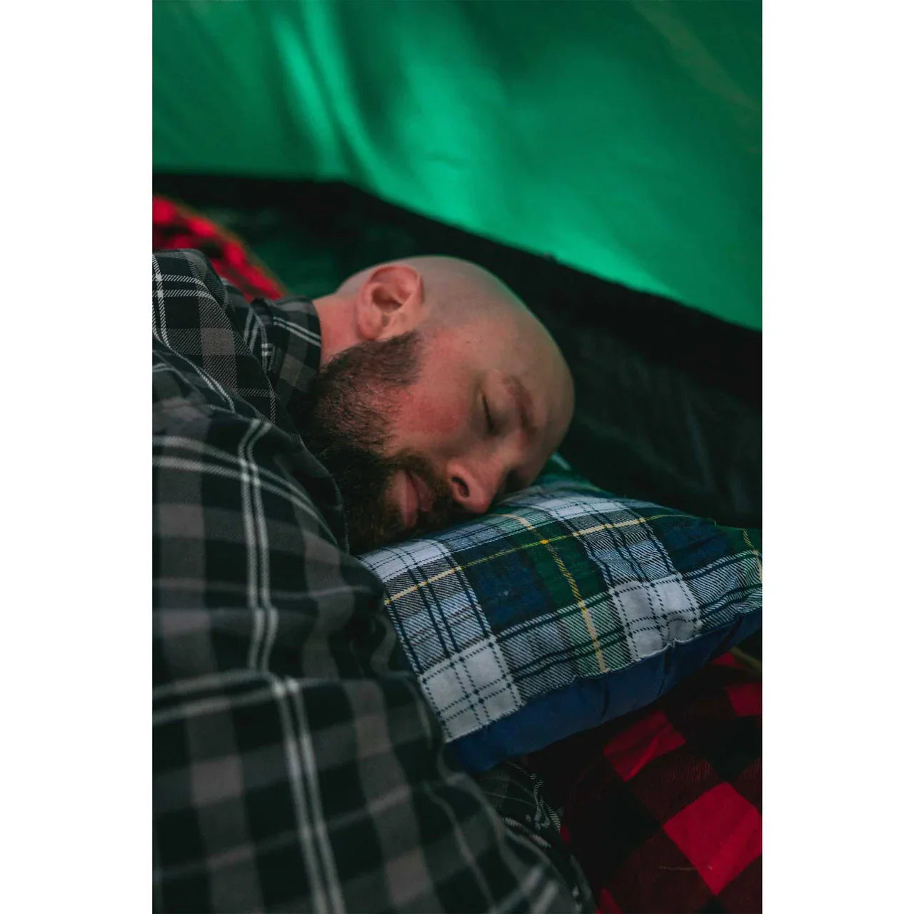 Man sleeping on plaid Stansport washable camp pillow inside a green tent