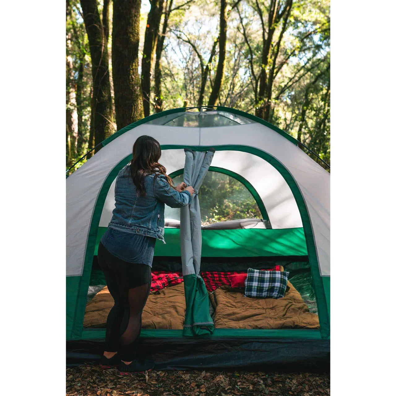 Woman opening tent flap, plaid camp pillow on sleeping bag, forest campsite background