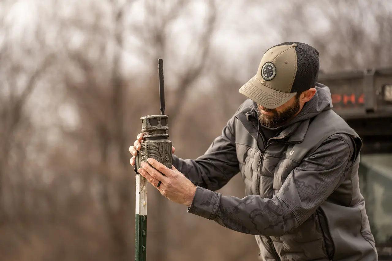 Man installing cellular trail camera on post outdoors in winter woods