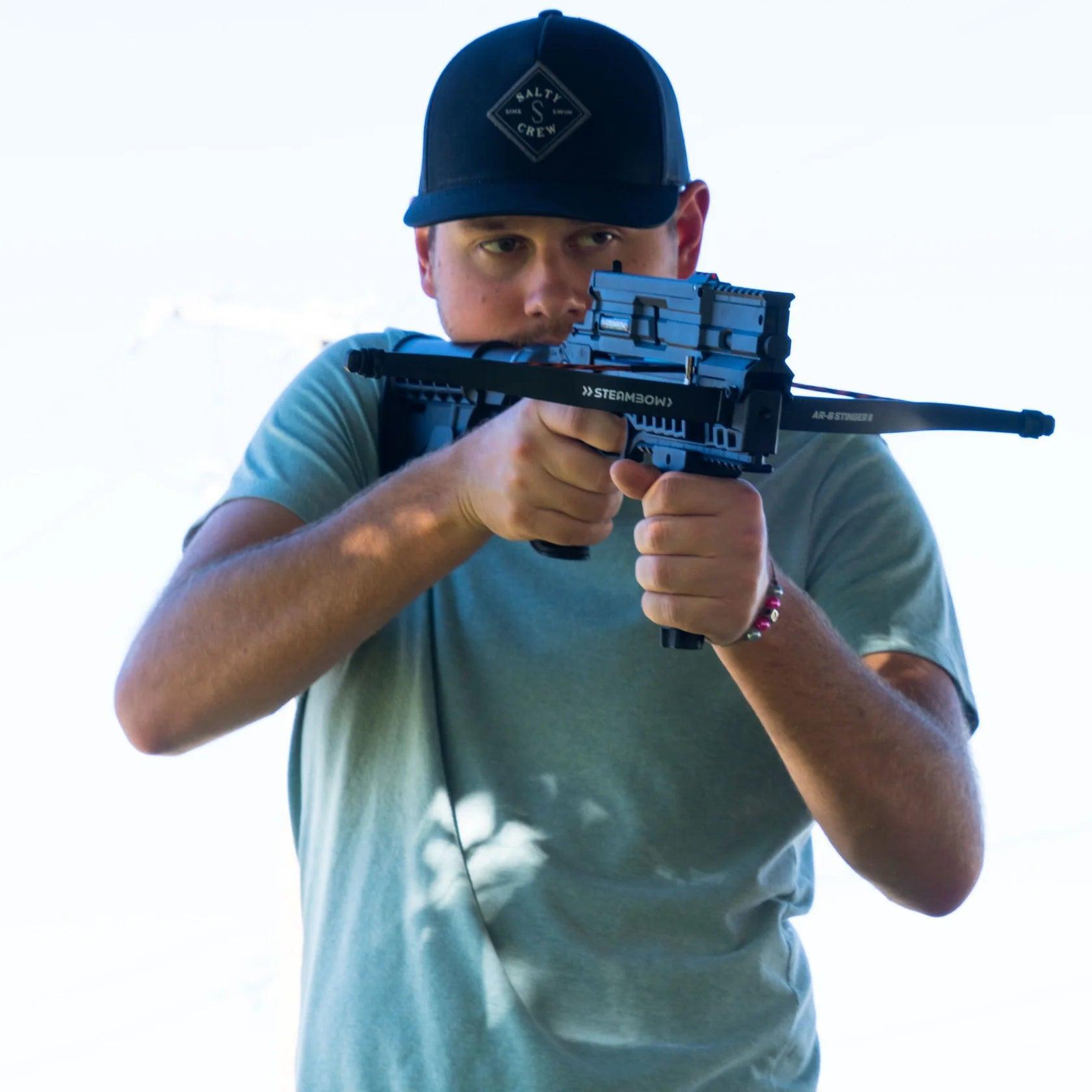 Man aiming Steambow AR-6 Stinger II tactical crossbow outdoors in daylight.
