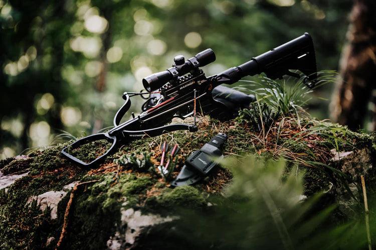 AR-6 Stinger 2 crossbow with scope resting on mossy rock in forest, survival gear nearby