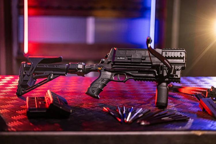 Tactical black airsoft rifle with magazine and darts on a metal table, colorful background lighting