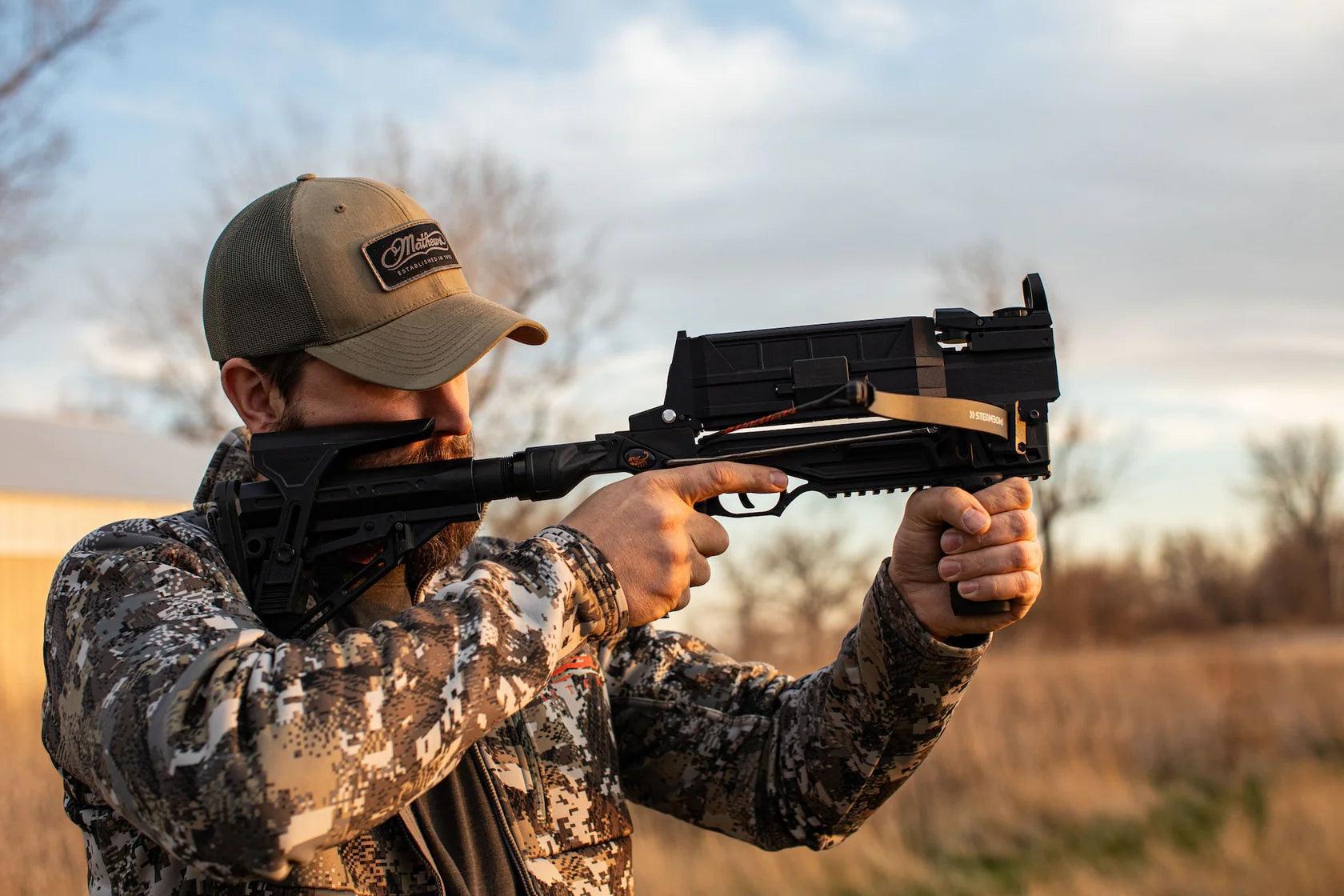Man aiming Steambow AR-Series M10 crossbow outdoors in camo jacket and cap
