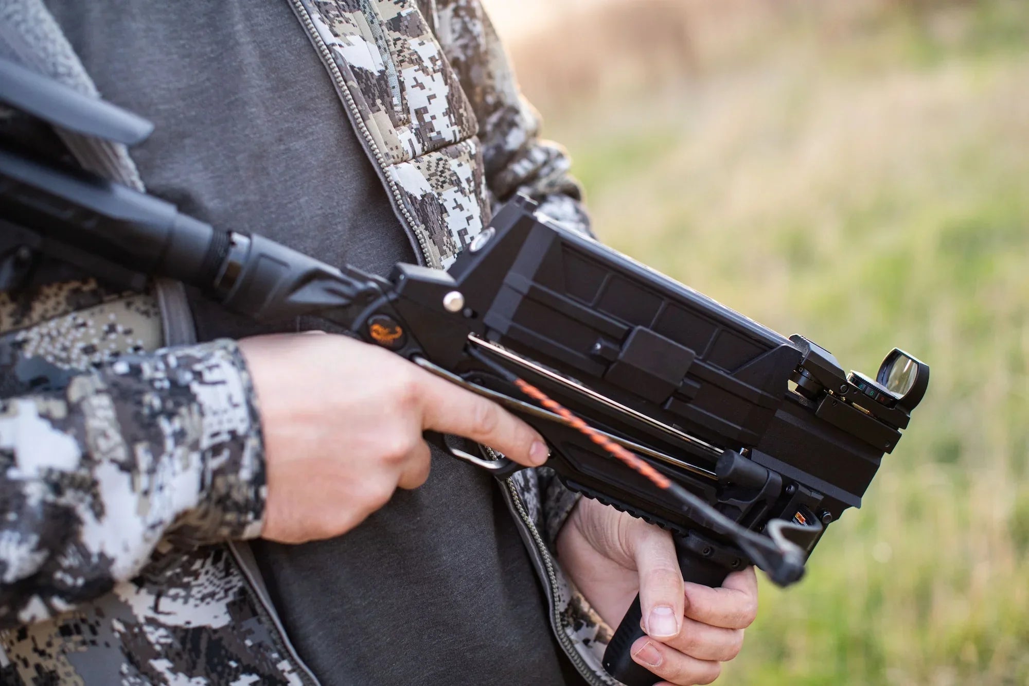 Person in camo jacket holding a black crossbow outdoors, hunting equipment detail