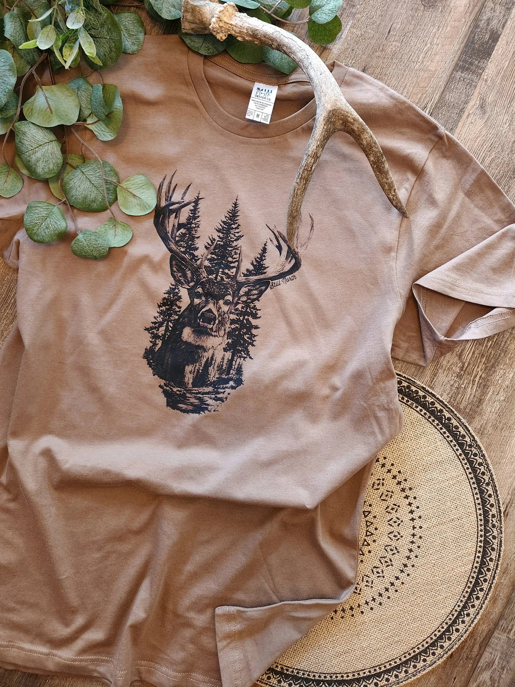 Brown graphic tee with deer and forest print, antler, leaves, rustic wood background