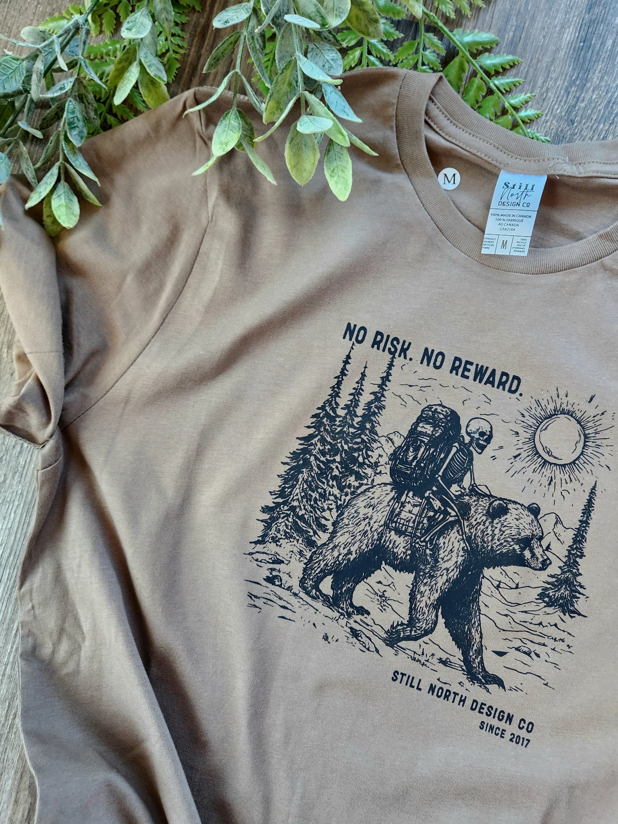 Brown Still North Design Co t-shirt with graphic of skeleton riding bear in forest, adventure theme