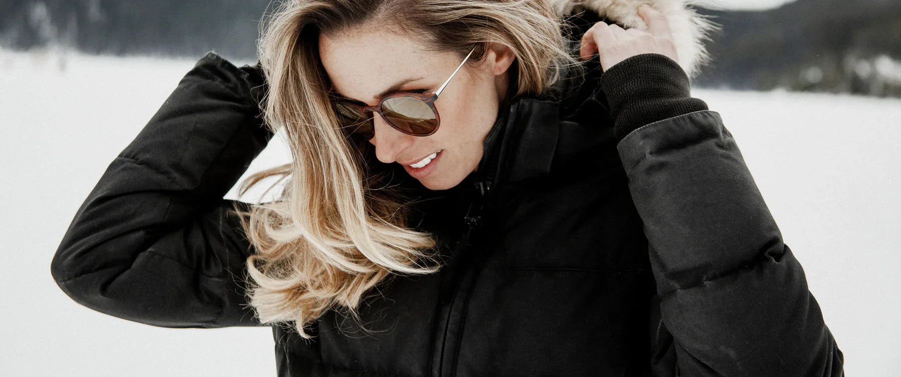 Woman in black winter jacket and sunglasses outdoors in snowy landscape