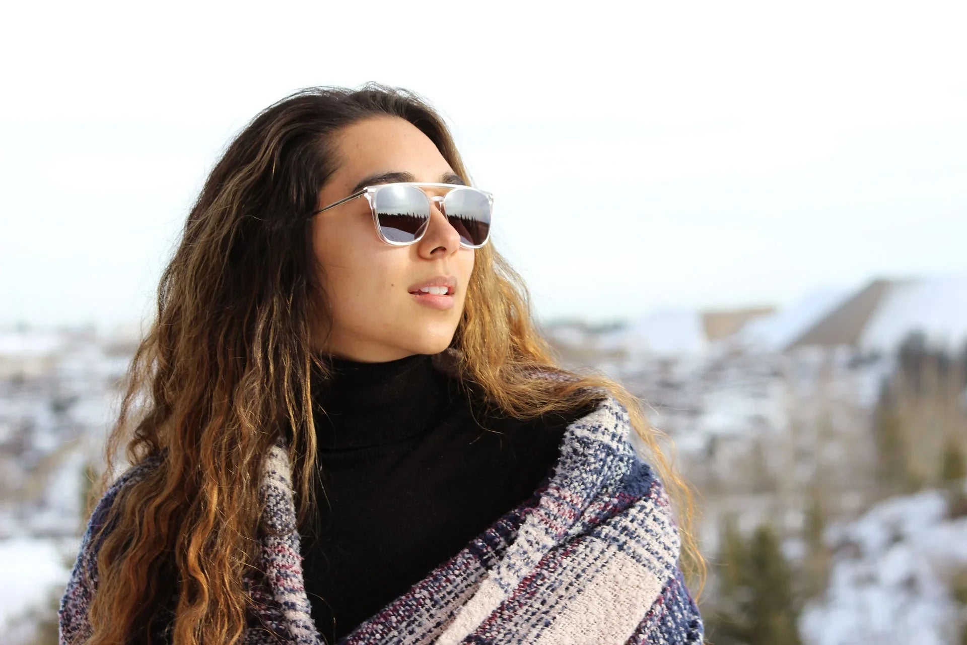 Woman in sunglasses and plaid shawl outdoors with snowy landscape background