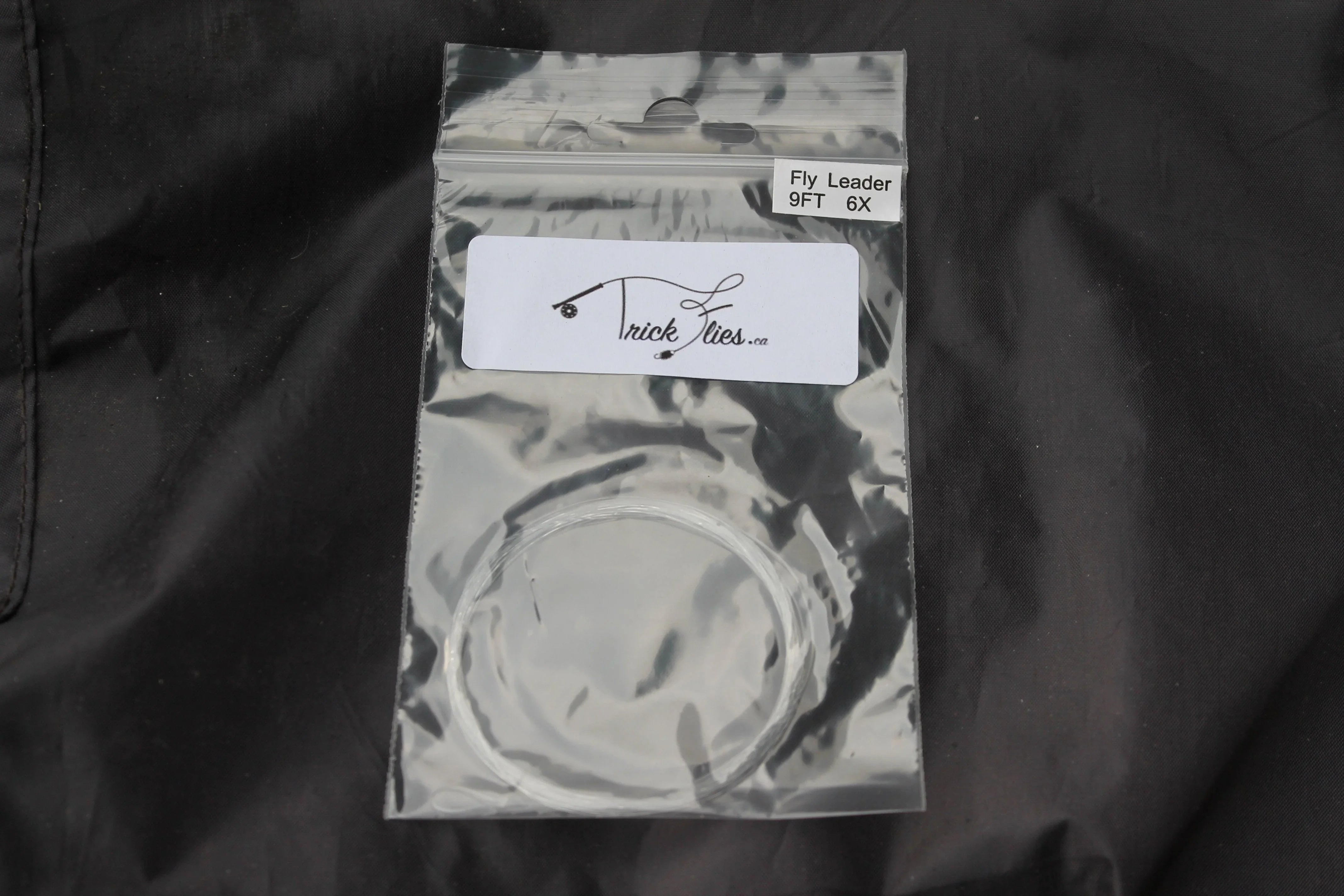Tapered fly fishing leader 9ft 6X in clear plastic bag with Trick Flies label on black fabric