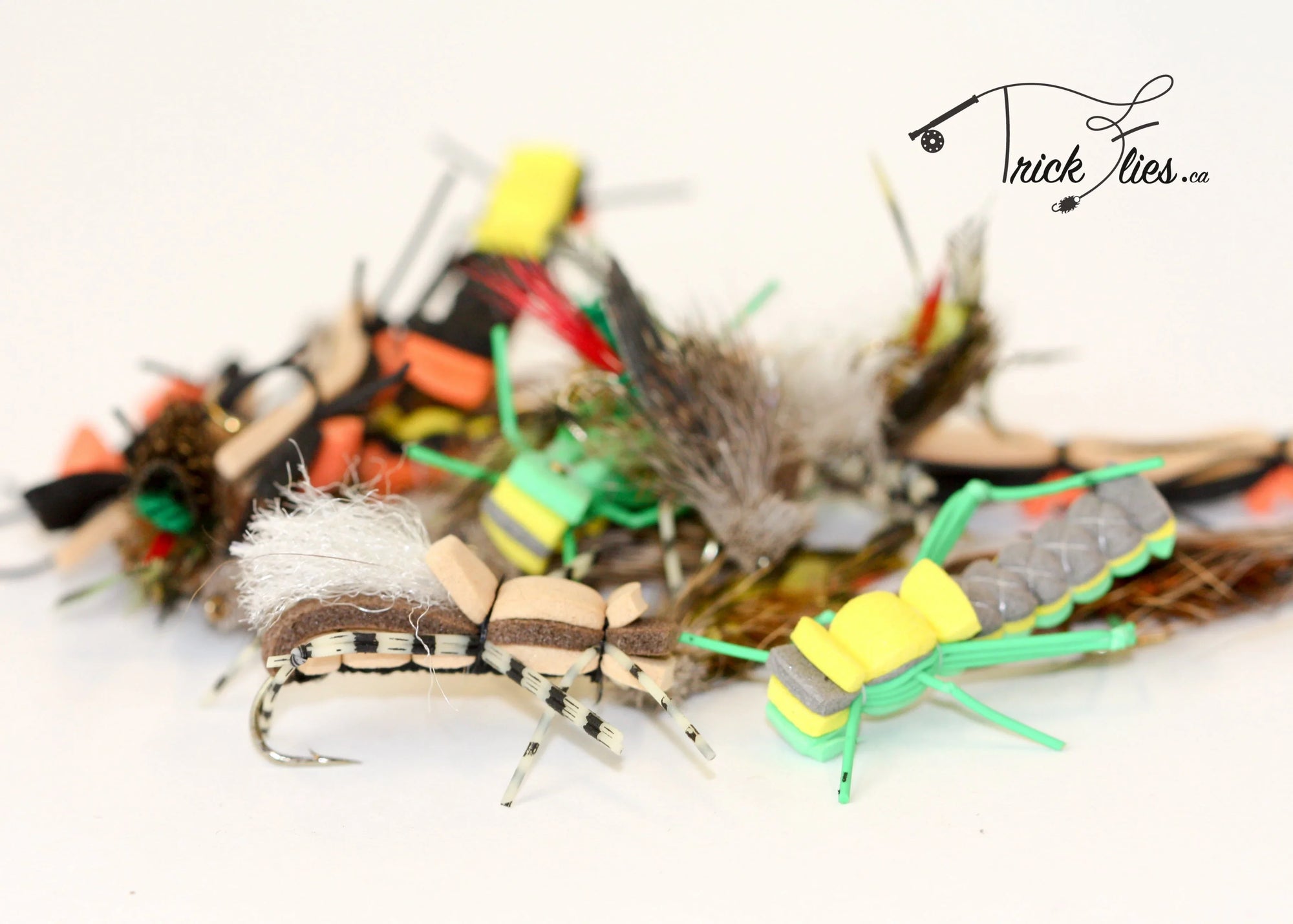 Assorted colorful foam fly fishing flies with hooks on white background, Trick Flies logo visible.