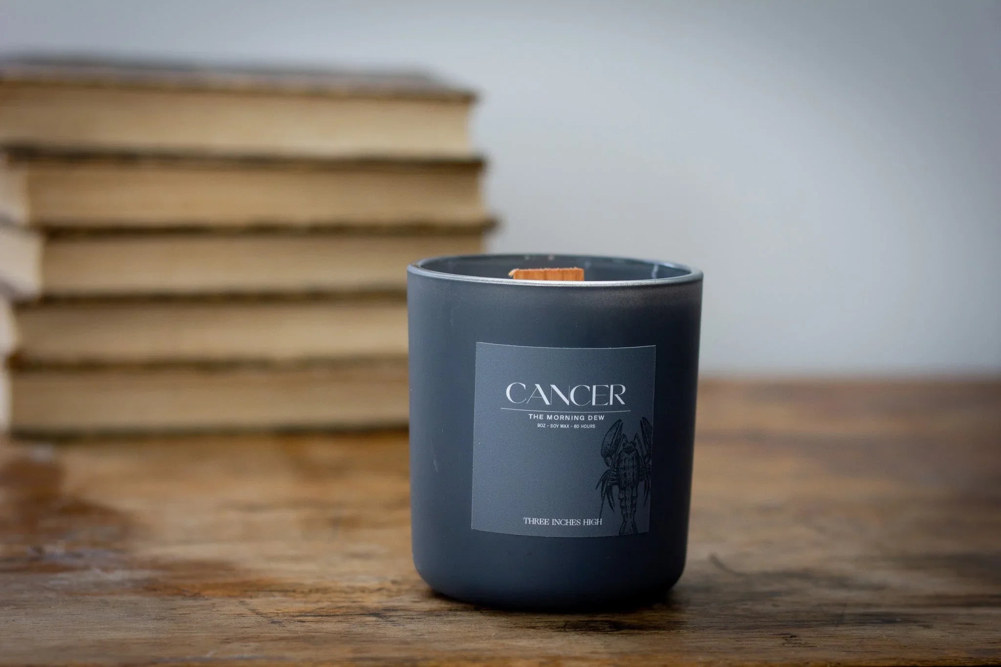 Cancer zodiac candle with dark glass jar on wooden table, books in background