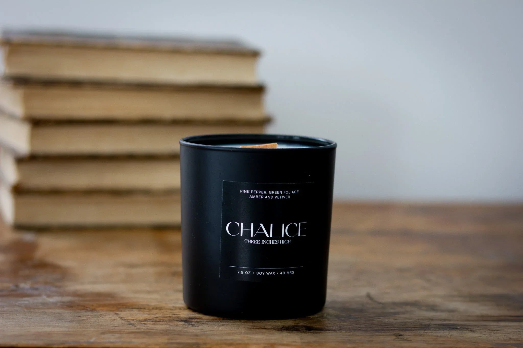 Black Chalice soy candle on wooden table with stacked books in background