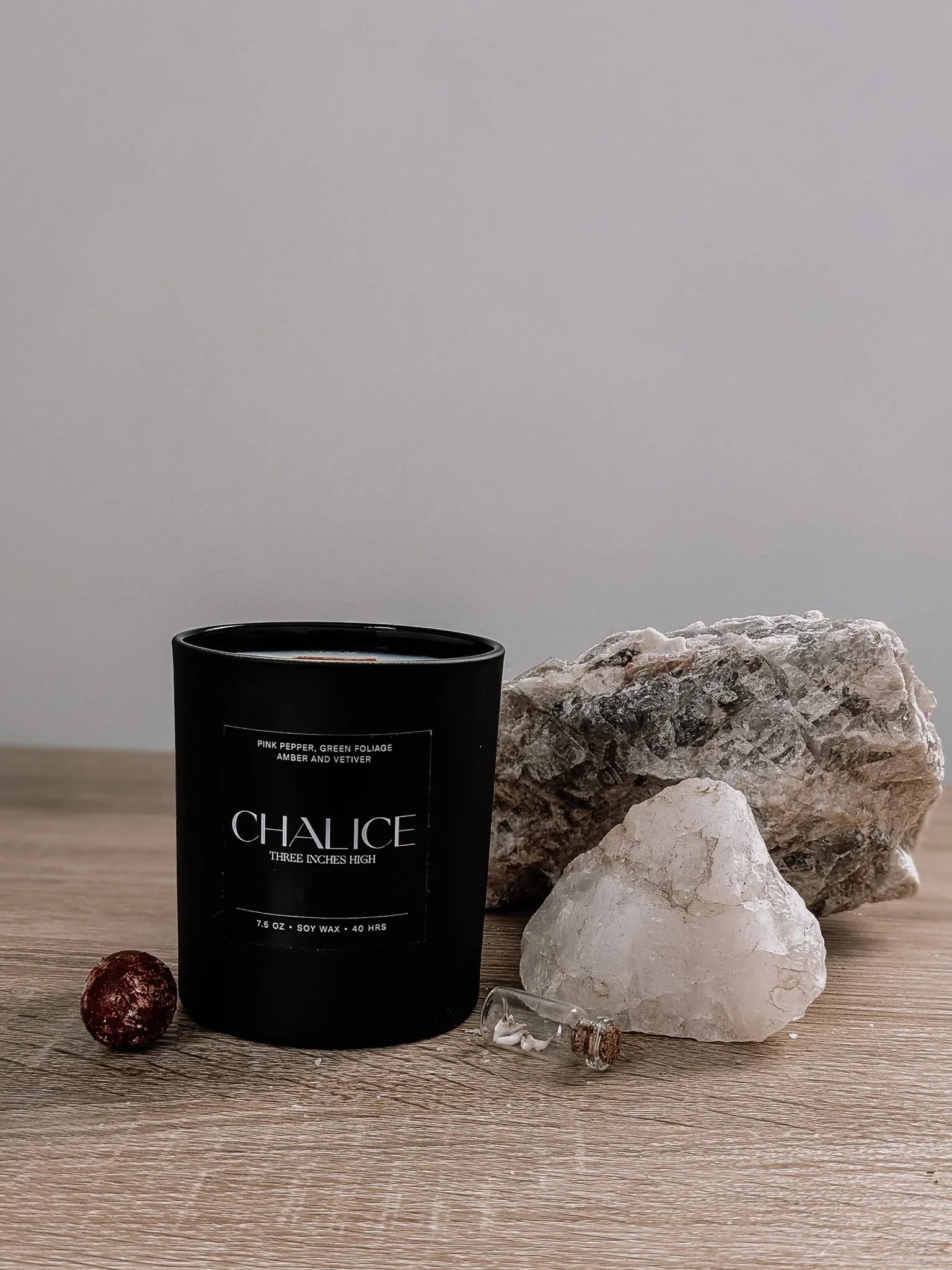 Black soy candle labeled Chalice on wood surface with crystals and stones