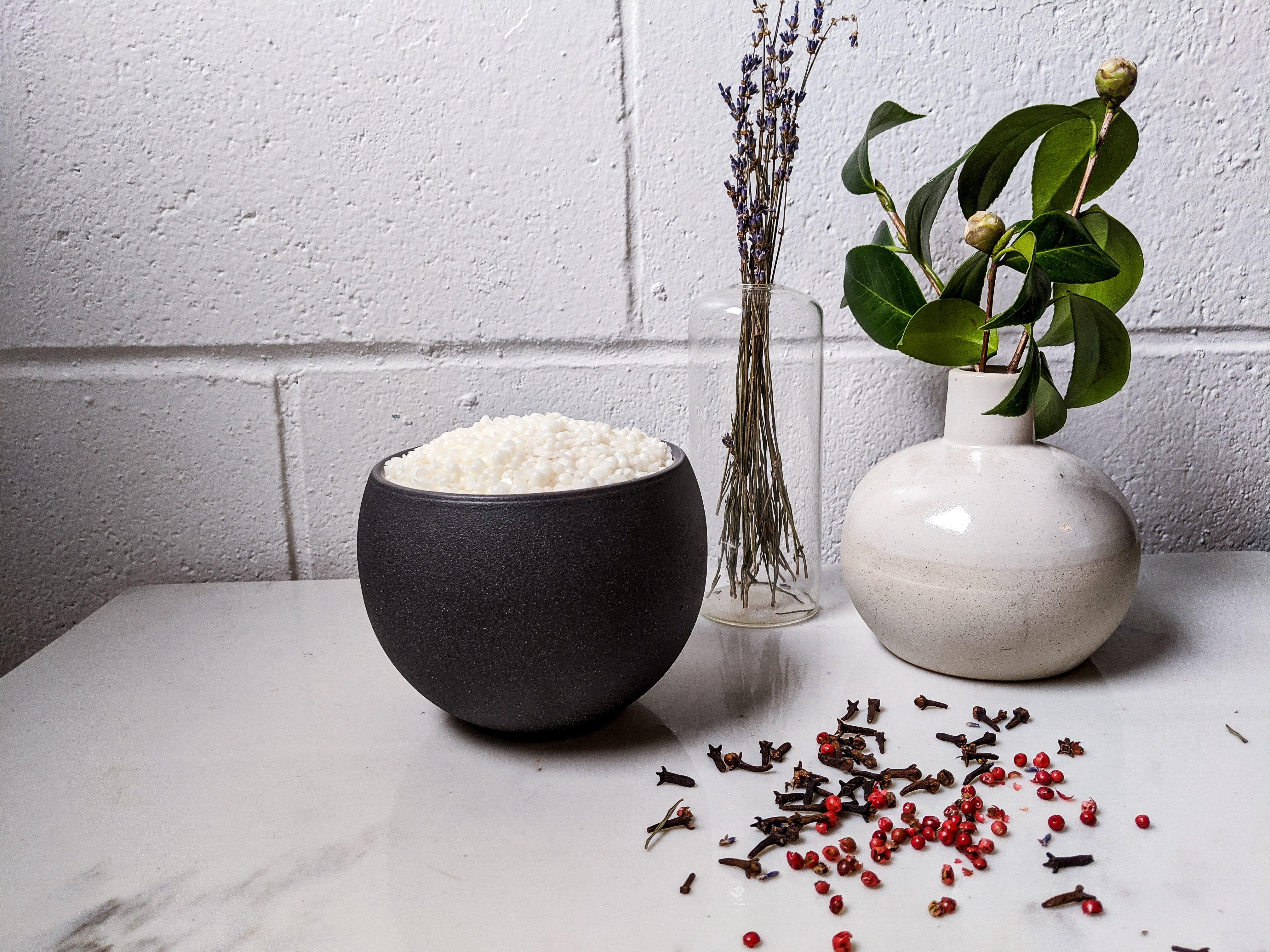 Black bowl filled with white pellets, vases with greenery, cloves, and pink peppercorns on white table