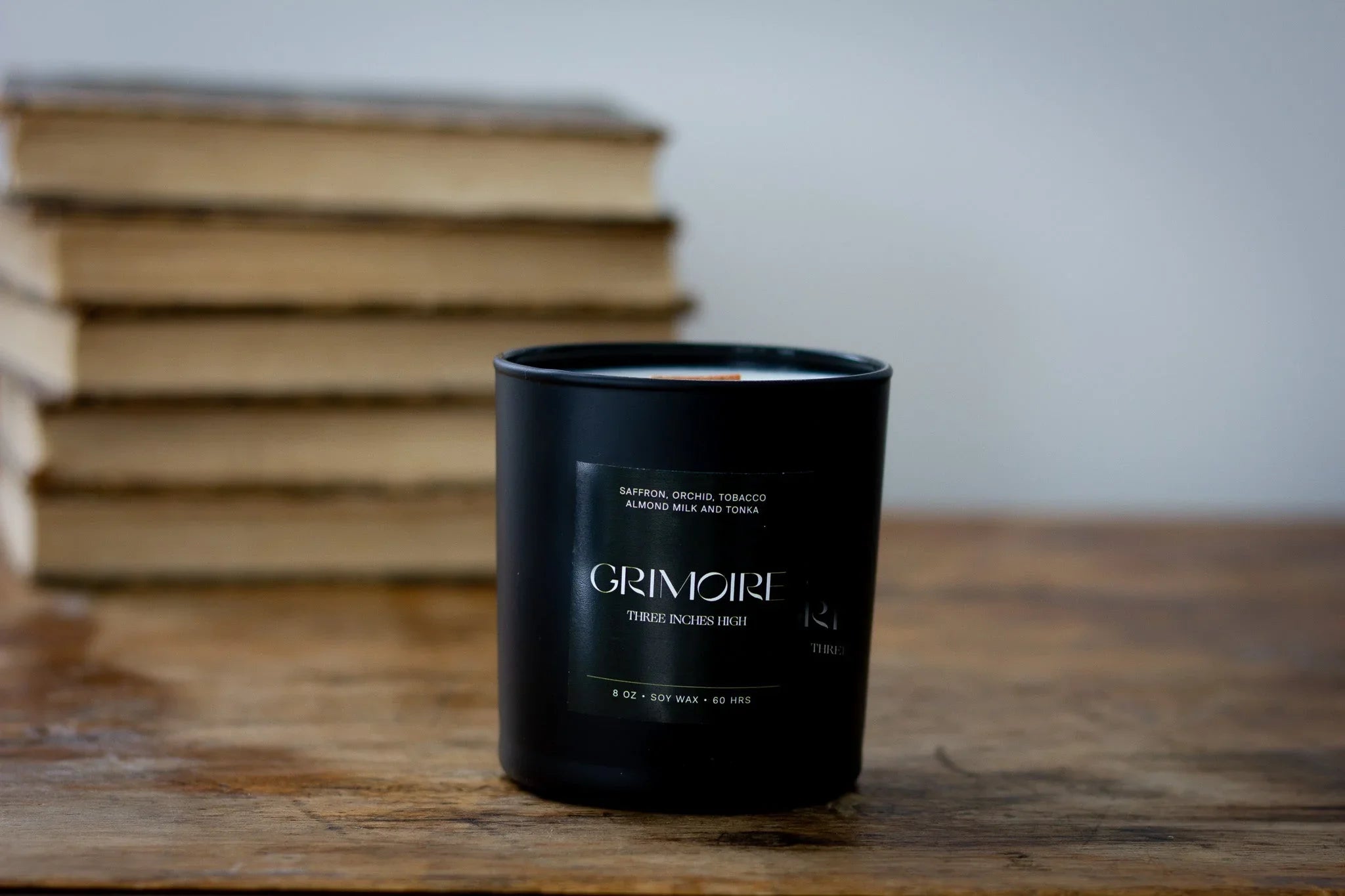 Grimoire scented soy candle in black jar on wooden table, stacked books in background