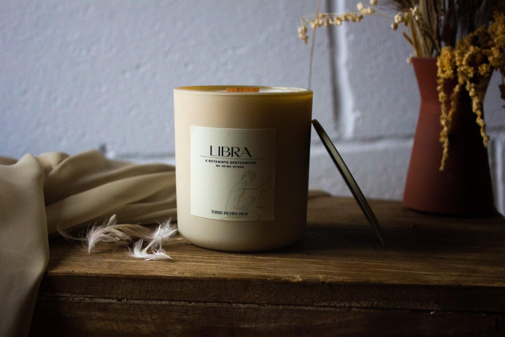Libra scented candle in cream jar on wooden table, dried flowers and fabric nearby