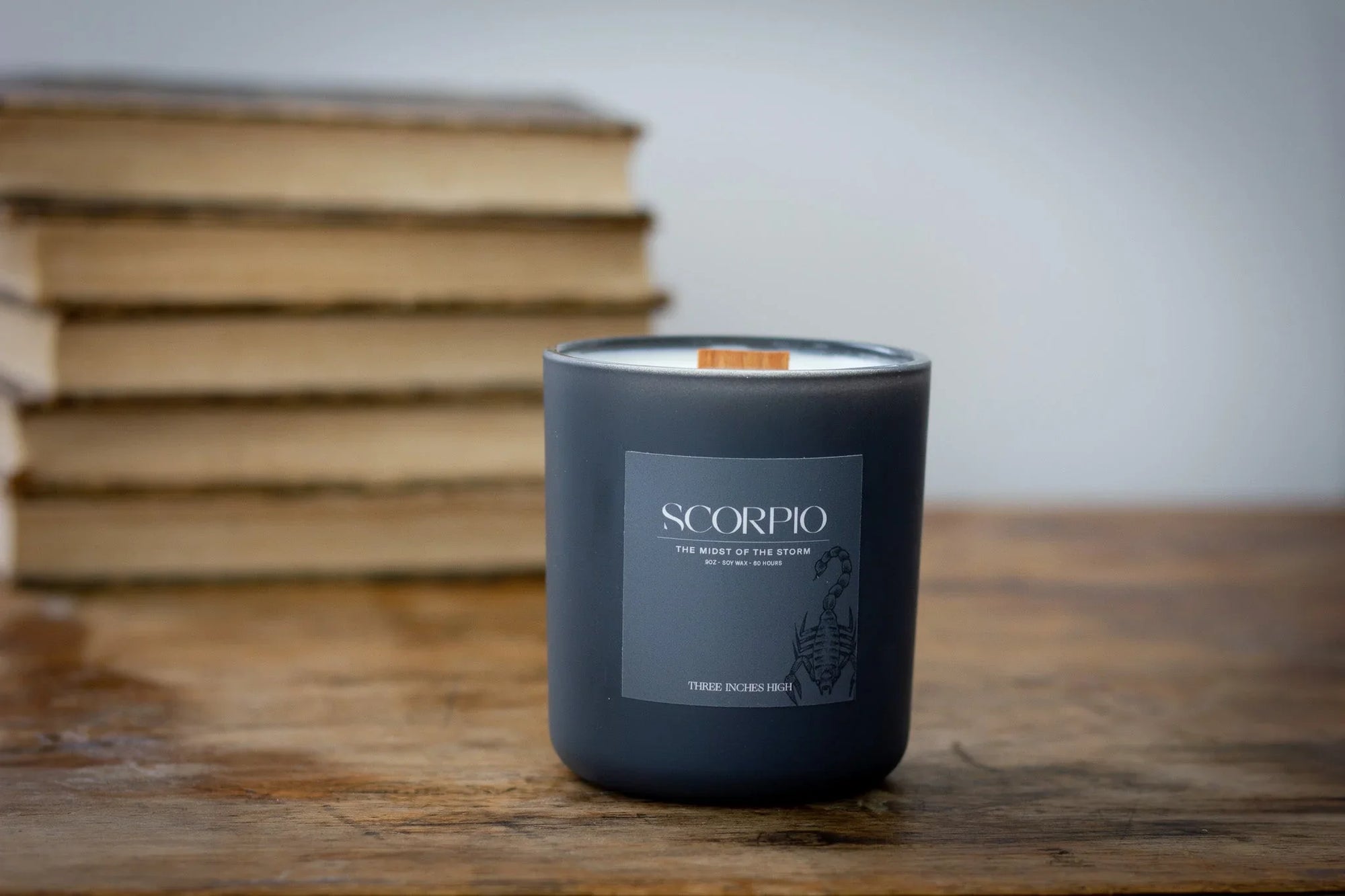 Scorpio zodiac candle in matte black glass jar on wooden table with books in background
