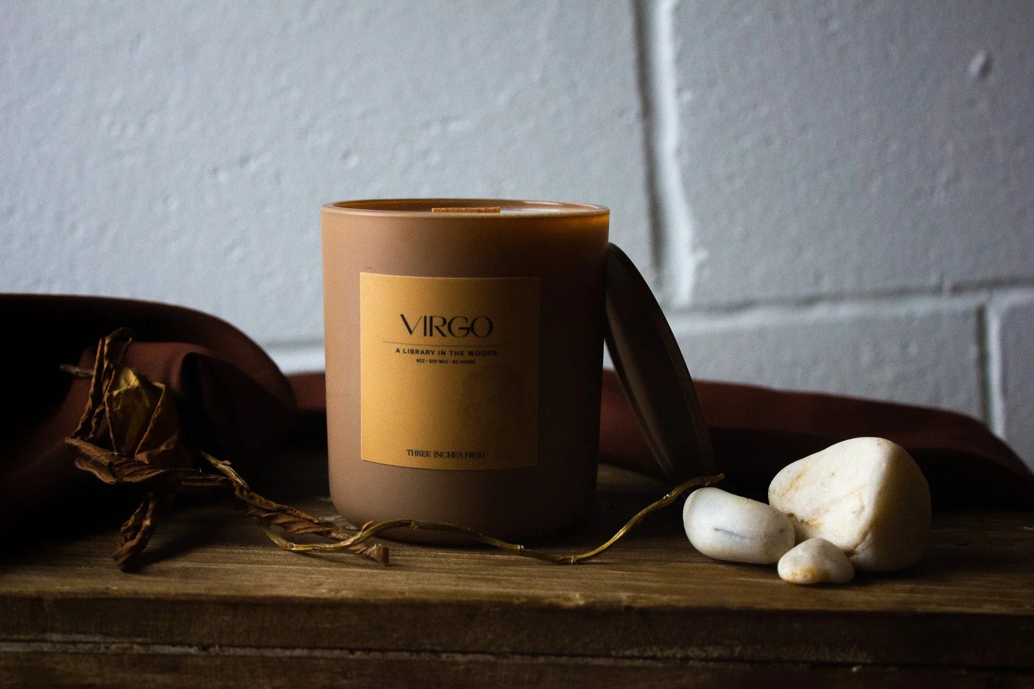 Virgo scented candle on rustic wood table with stones and dried leaves, minimalist decor