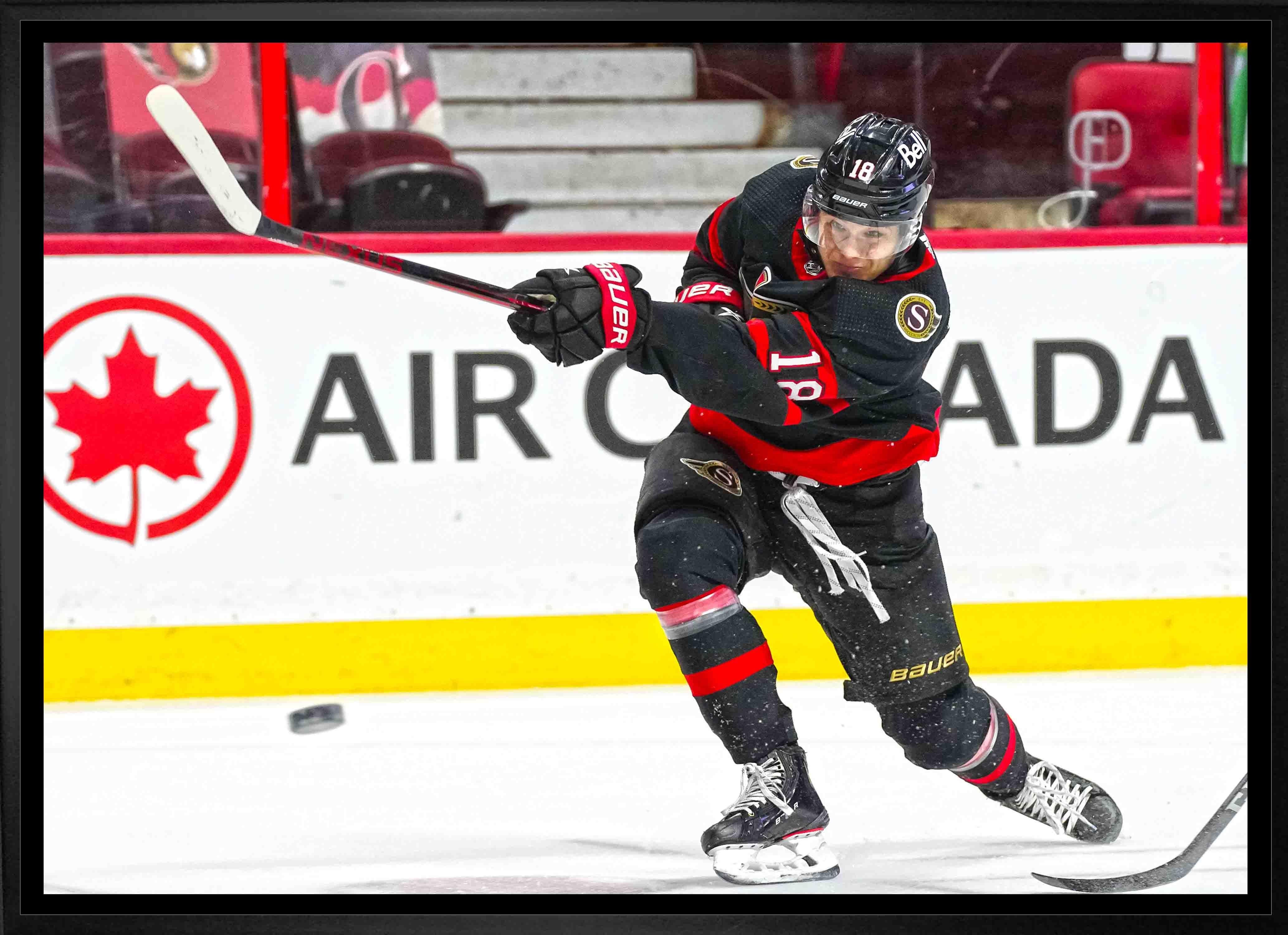 Ottawa Senators hockey player in black uniform taking a slap shot on ice rink