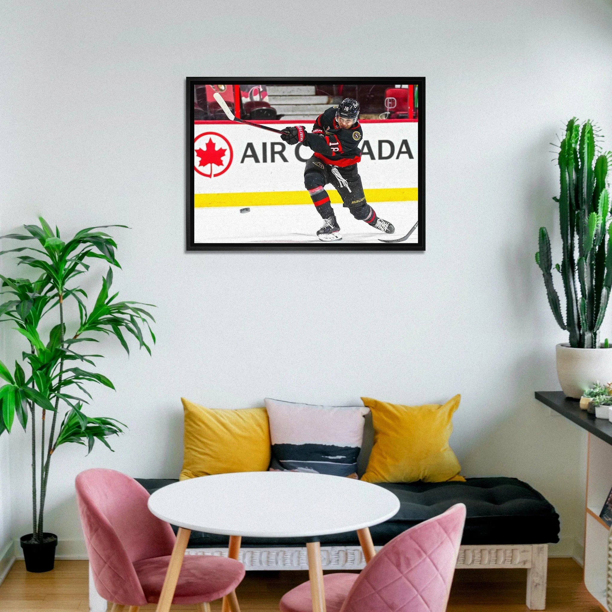 Modern living room with framed hockey player art, round table, pink chairs, and green plants