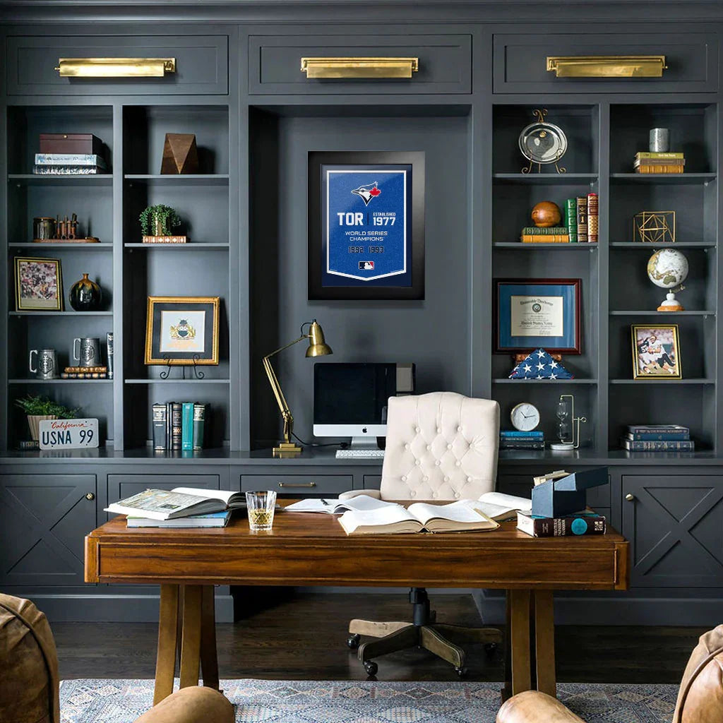 Modern home office with dark built-in bookshelves, wooden desk, computer, and framed Toronto Blue Jays print.