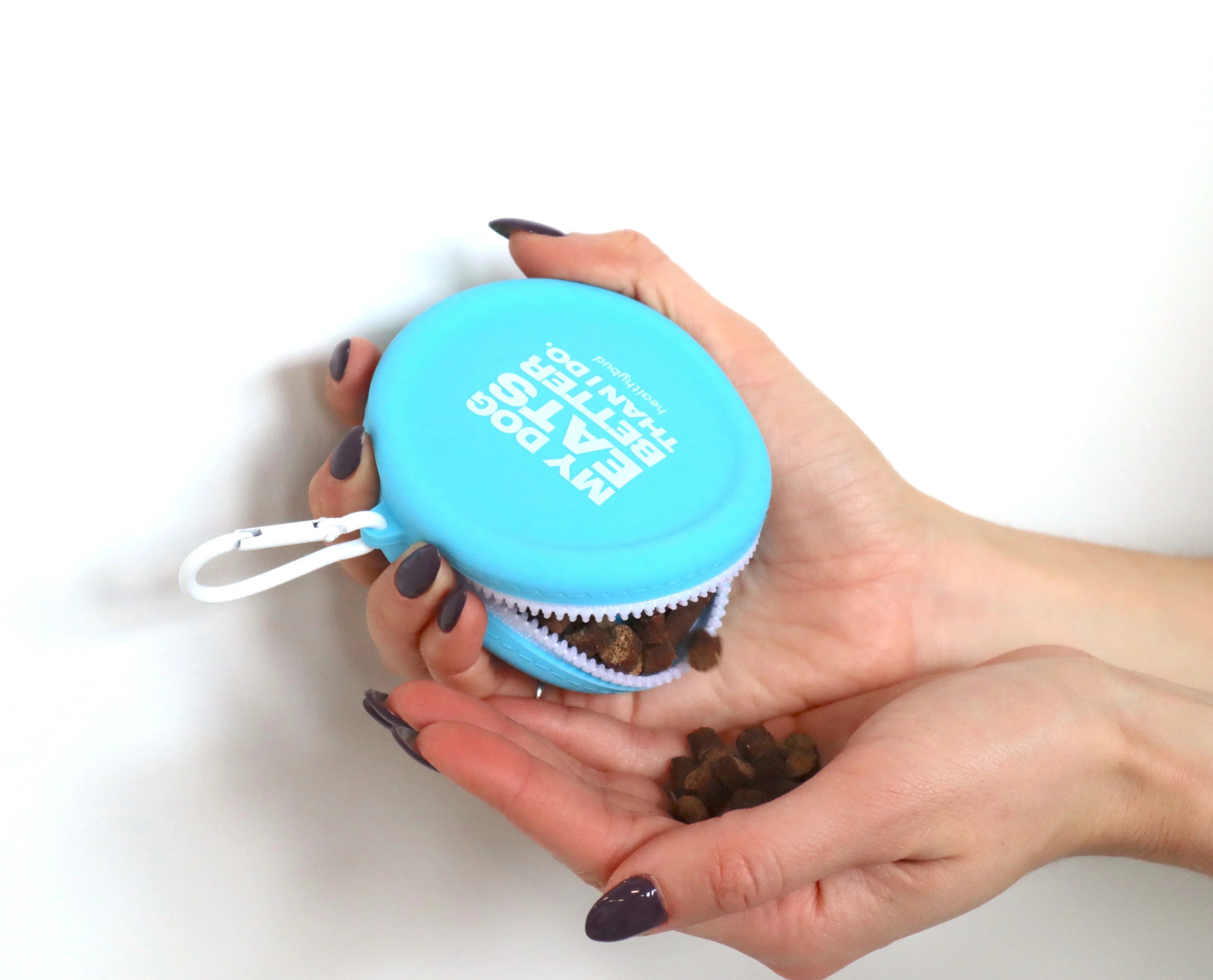 Blue dog training treat pouch spilling kibble into a person's hand on white background