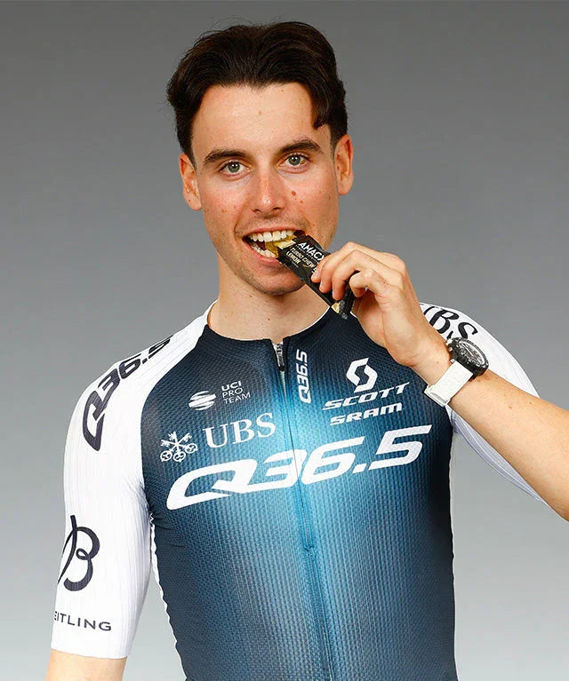 Male cyclist in Q36.5 team kit eating Turbo Chew Bar Lemon energy bar, gray background