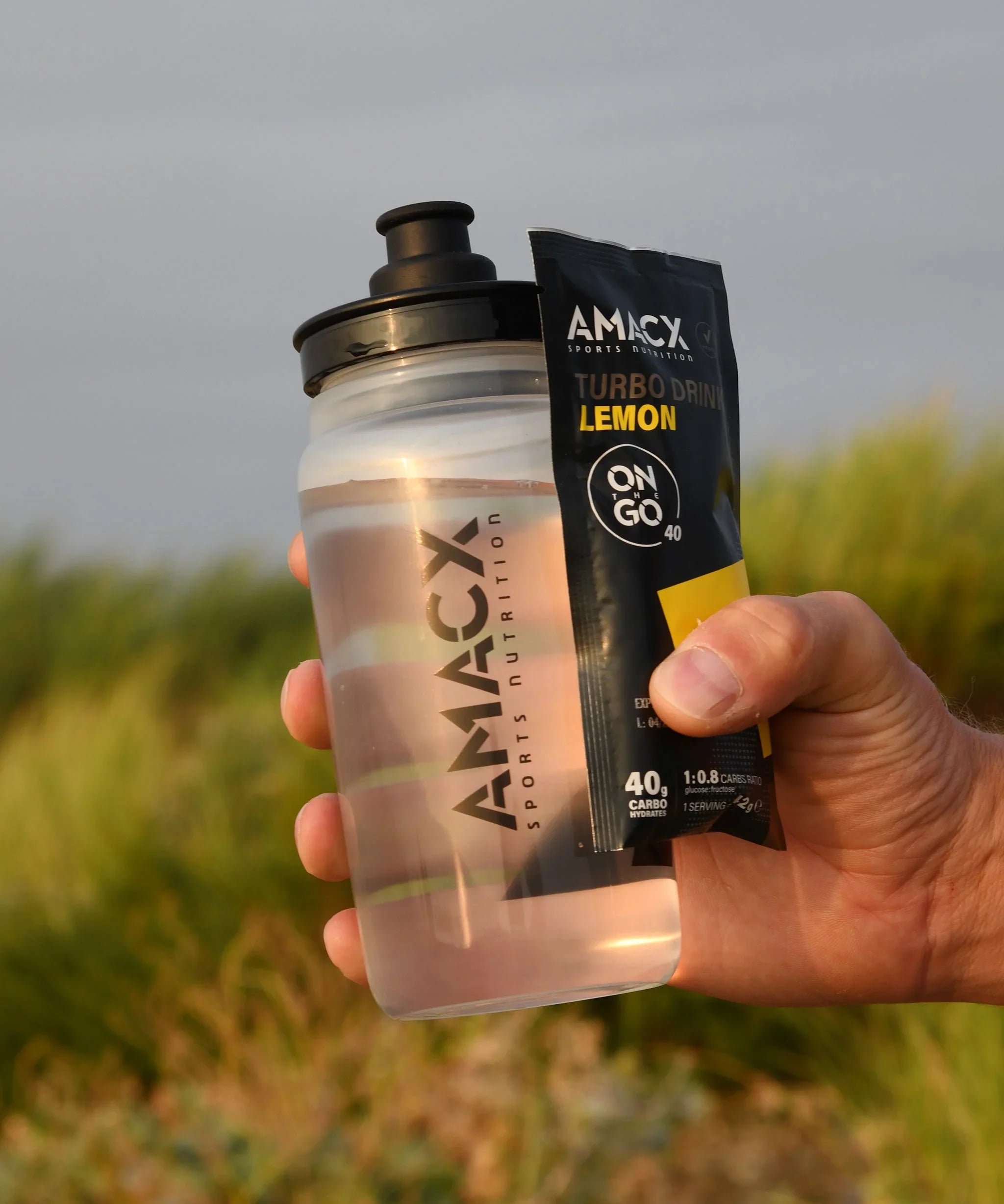 Hand holding AMACX sports nutrition water bottle and Turbo Drink Lemon sachet outdoors