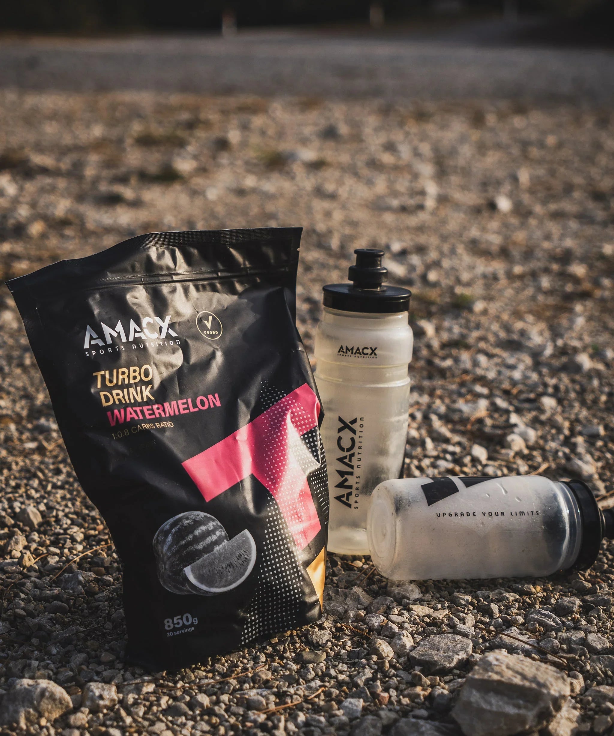 AMACX Turbo Drink Watermelon powder and two sports bottles on gravel outdoors