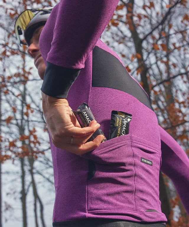 Cyclist in purple jersey placing energy bars in back pocket, outdoors in autumn woods