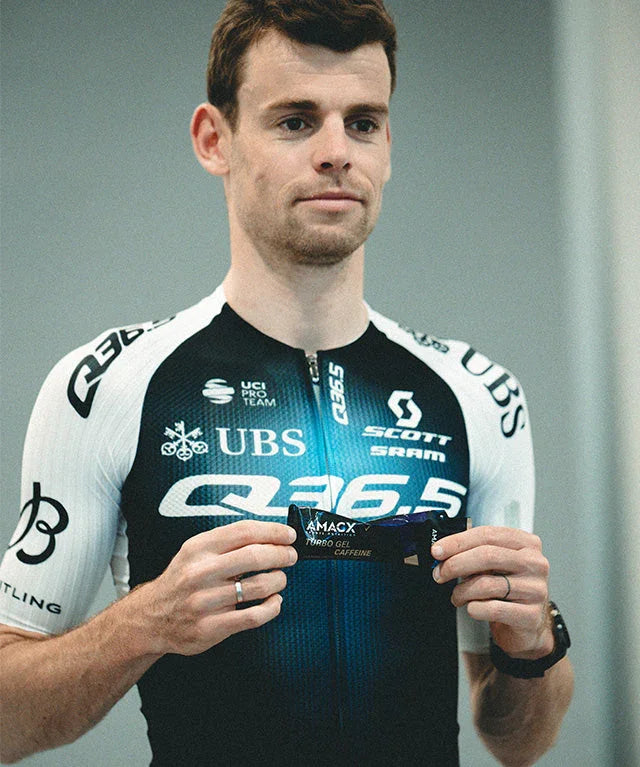 Male cyclist in Q36.5 team jersey holding Amacx Turbo Gel Caffeine energy gel