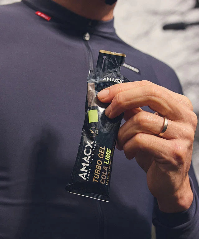 Hand holding AMACX Turbo Gel Cola Lime energy gel sachet, close-up, sport apparel