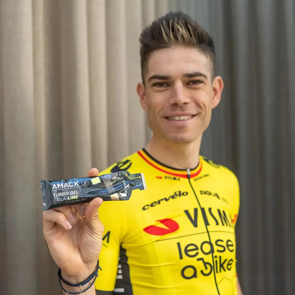 Cyclist in yellow Visma jersey holding Amacx Turbo Gel Cola Lime energy gel packet