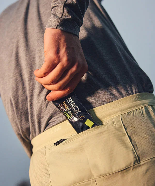 Runner placing Amacx Turbo Gel Cola Lime energy gel in pocket, outdoor sportswear focus