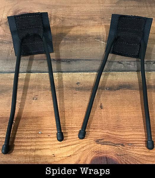 Two black spider wraps weapon attachments on wood surface, outdoor sports gear.