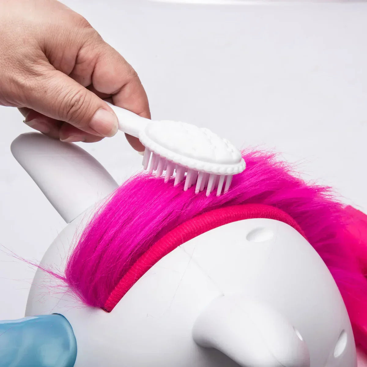 Brushing bright pink mane on white unicorn toy with small white brush