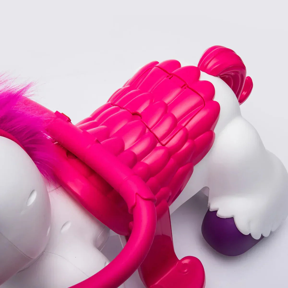 White unicorn toy with bright pink wings, tail, and mane, and purple hoof on white background