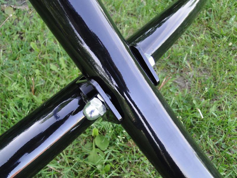 Close-up of black steel hammock chair stand joints and bolts on green grass outdoors