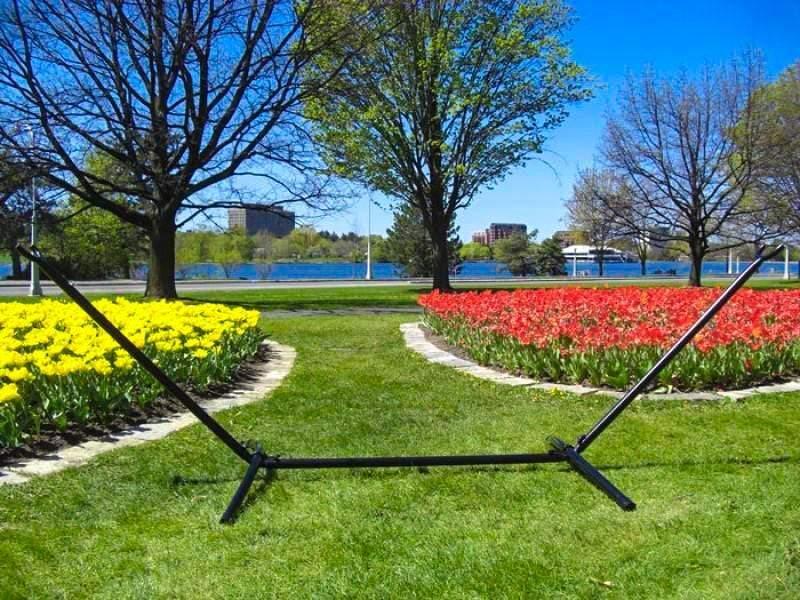 Universal hammock stand on grass lawn with blooming red and yellow tulip flowerbeds in park