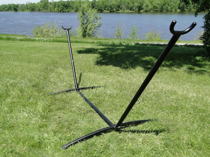 Black universal hammock stand on grass near river with trees in background outdoors