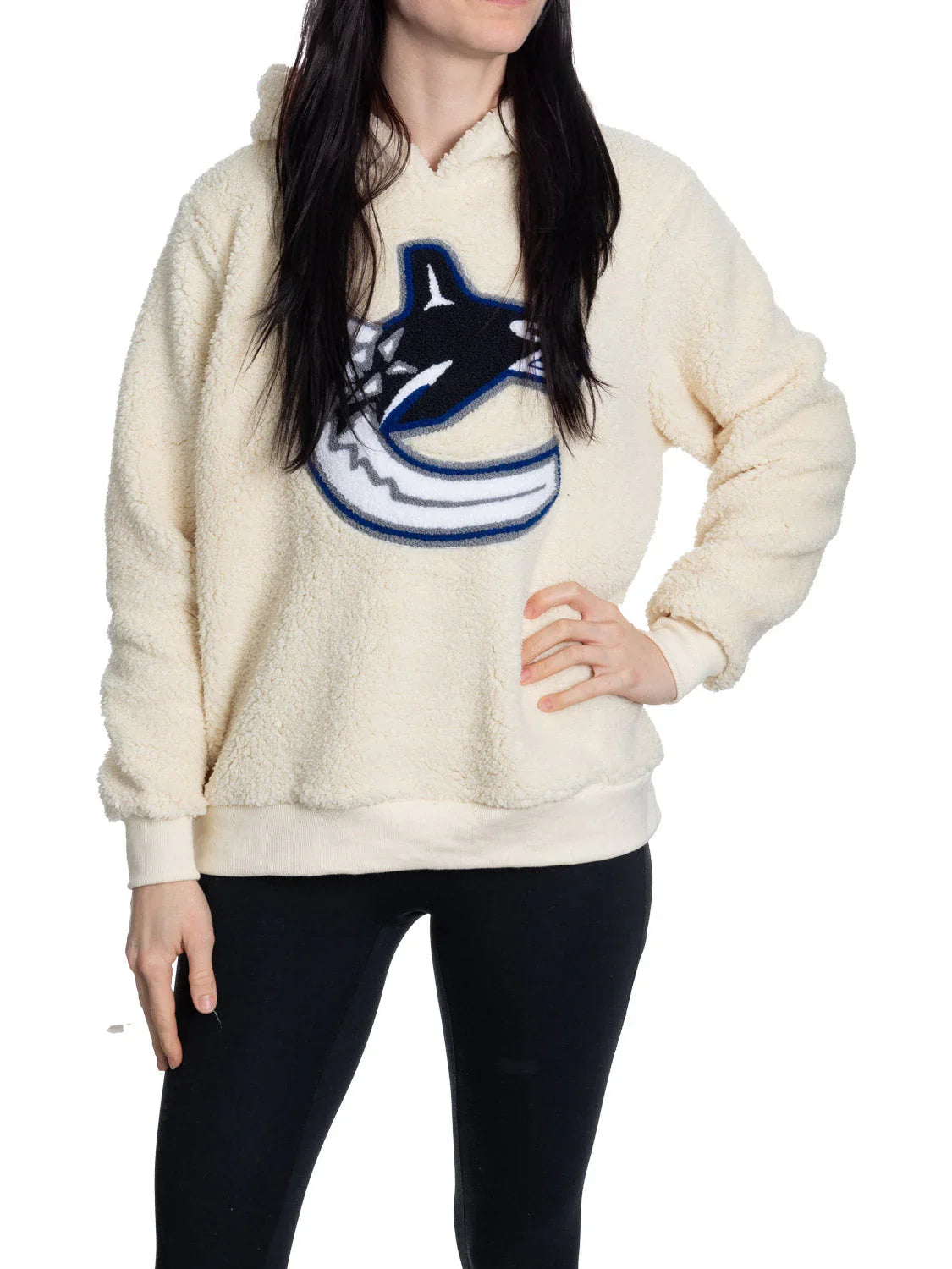 Woman wearing cream Vancouver Canucks sherpa hoodie with logo, black pants, white background