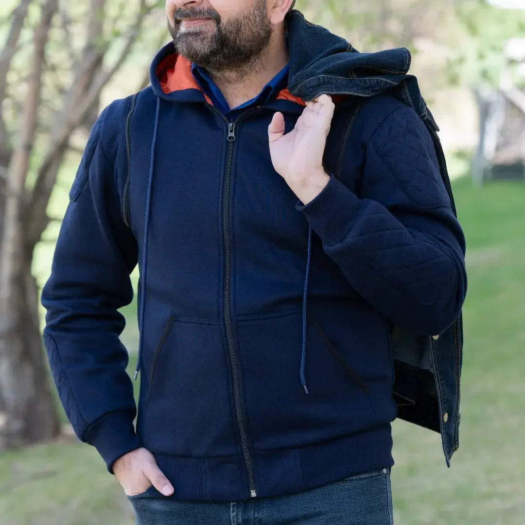 Man wearing navy blue zip-up hoodie with orange lining and denim vest outdoors