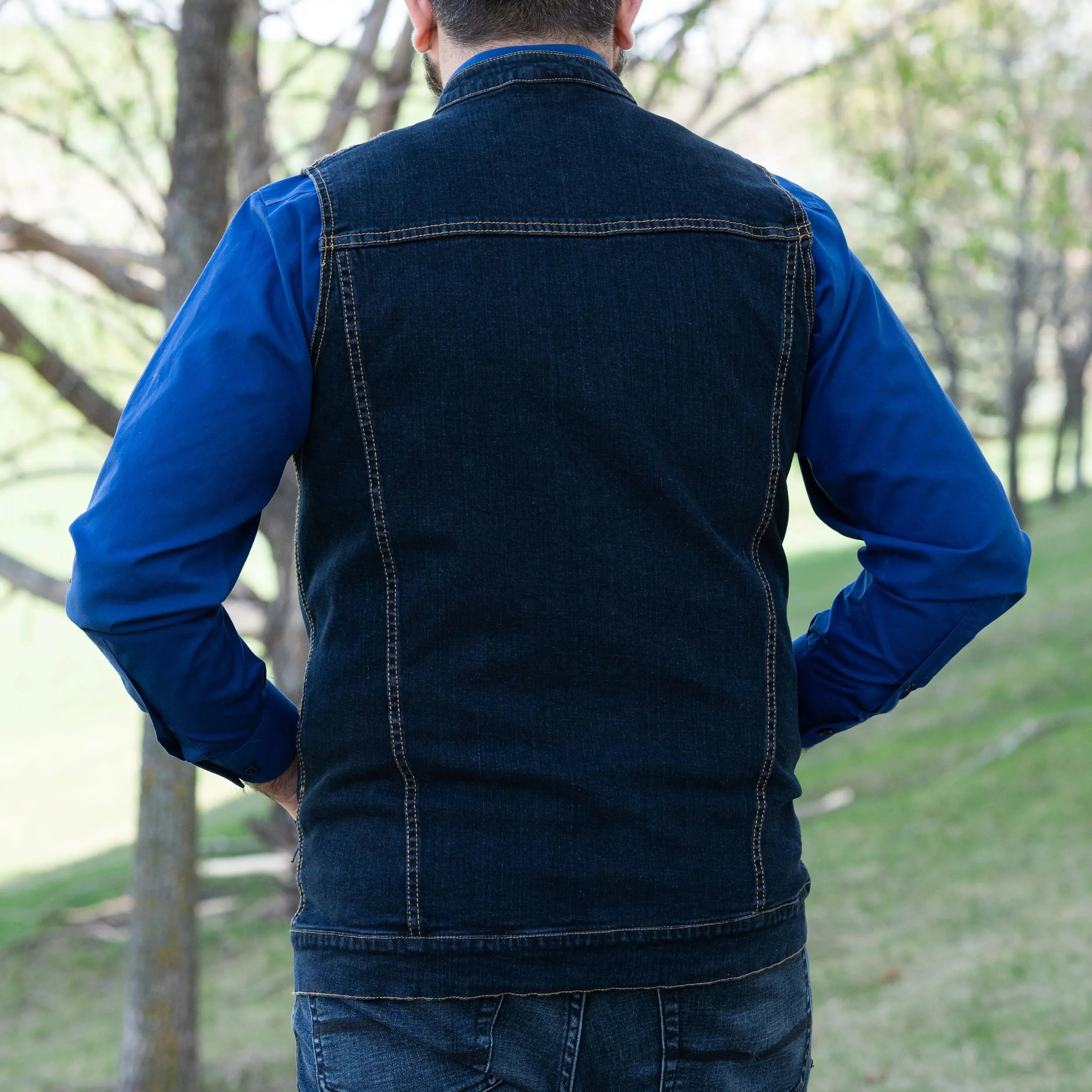Man outdoors wearing a blue denim vest over a blue shirt, back view, casual fashion